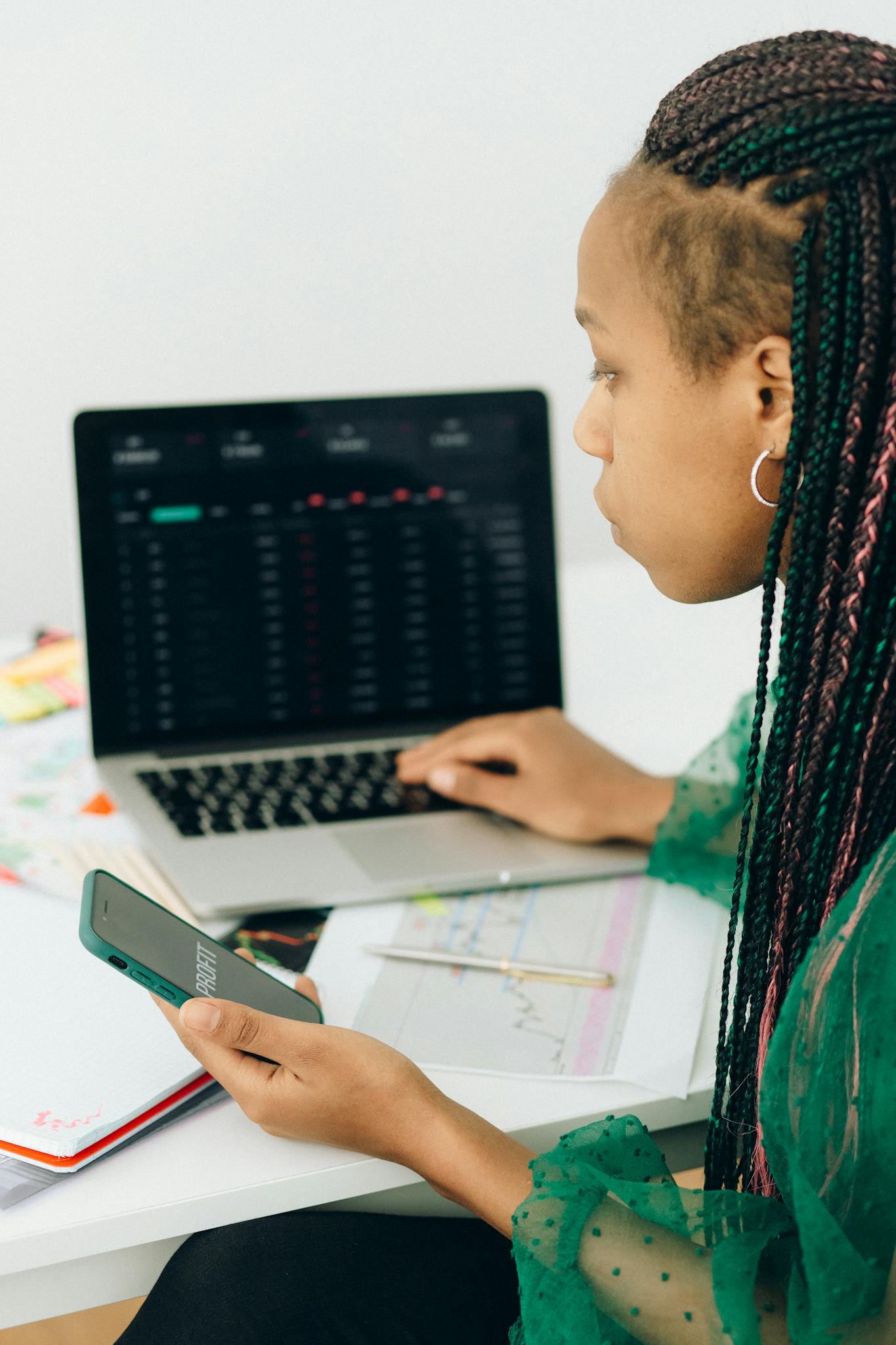 focused woman working with financial data on laptop and smartphone in modern office. 7172864 1365x2048