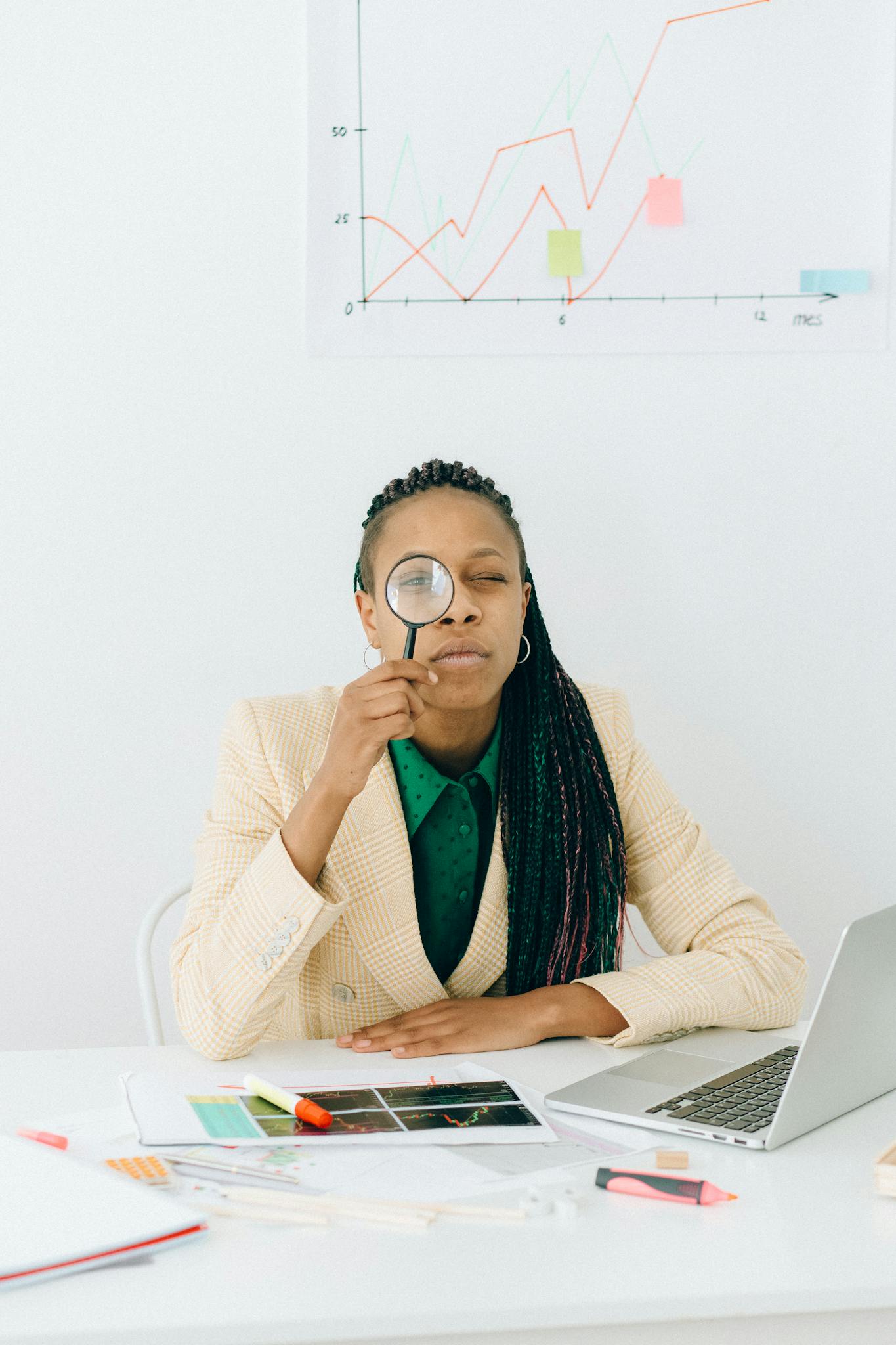 woman examining data charts with a magnifying glass at a desk with a laptop showcasing analytical skills. 7172982 1365x2048